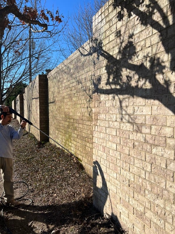 Long brick perimeter wall being pressure washed, stained and weathered