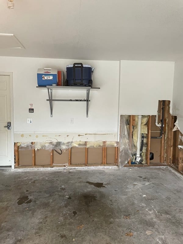 Garage wall with the lower drywall cut away, studs, pipes and insulation exposed
