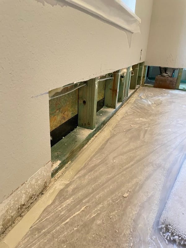 Damaged drywall cut away along the base of a wall, exposing the studs